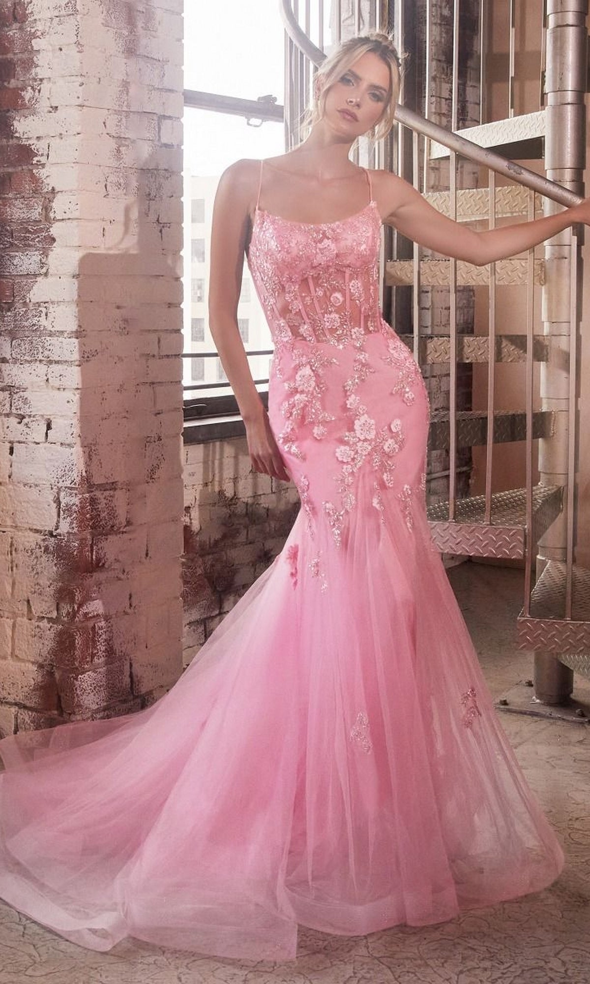 A woman poses by a spiral staircase in an industrial setting, wearing the Long Pastel Floral Mermaid Prom Dress D145—a fitted, floor-length gown with delicate embellishments.